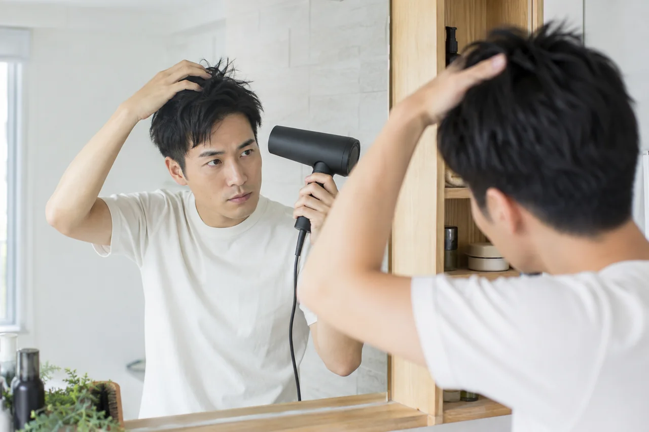 自宅の鏡の前で短髪の根元を手で持ち上げながらドライヤーを使う生成イメージ